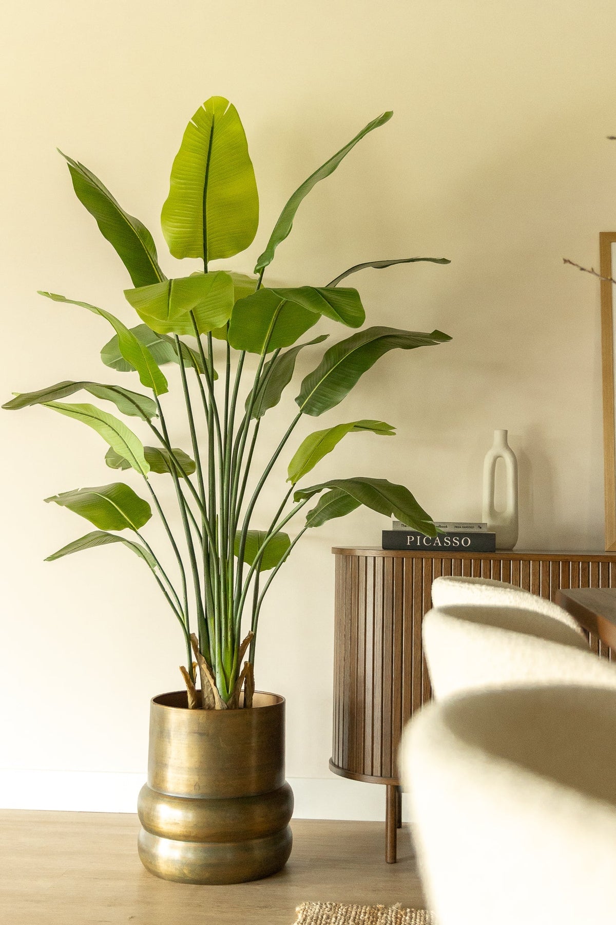 Strelitzia kunstplant in een messingkleurige pot in een lichte woonkamer